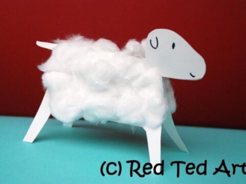 A simple craft of a sheep made from white cotton balls and paper. The sheep stands on a blue surface with a red background. The © Red Ted Art is visible in the corner.