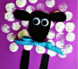 A craft depicting a sheep made from a black spoon for the body and wine cork stamps for wool, with a blue polka dot ribbon around its neck. The background is a purple surface, and the text Wine Cork Sheep is at the bottom.