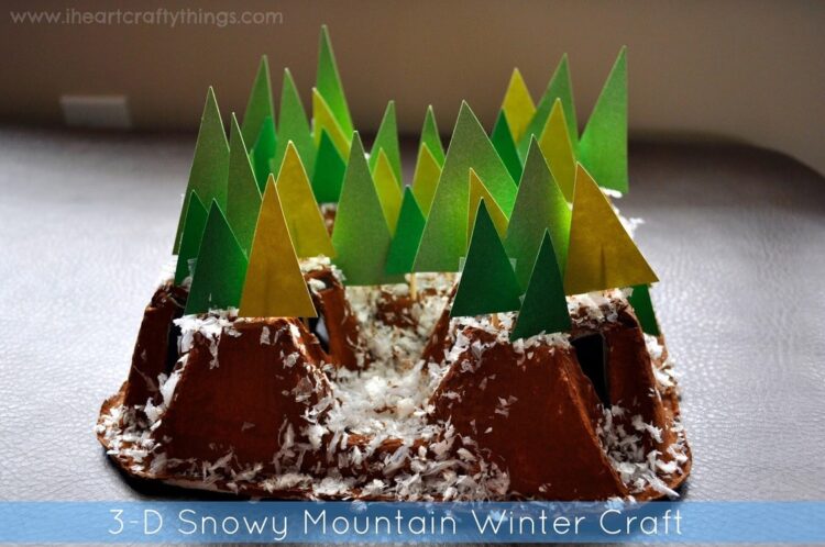 A 3D winter craft featuring brown paper mountains with green and yellow paper trees. Snow-like material is scattered on the mountains, creating a snowy scene. Text reads 3-D Snowy Mountain Winter Craft.