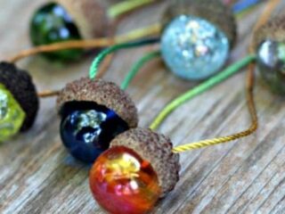 Close-up of colorful marbles set in acorn caps, attached to cords, resting on a wooden surface.