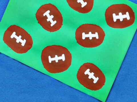 A green paper features several brown football shapes stamped in a grid pattern using potatoes. Each football has white laces painted on top. The words Potato Stamped Football are written at the bottom.