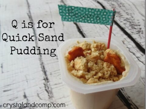 A container of pudding topped with crumbled cookies and small pretzels. A decorative flag sticks out of the pudding. The text reads, Q is for Quick Sand Pudding. The website URL is crystalandcomp.com.