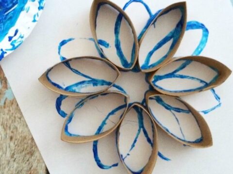 A flower-shaped design made from brown, paper roll pieces arranged in a circle on white paper. Blue paint outlines the shapes, creating a decorative effect.