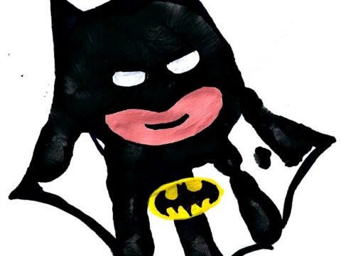 A handprint art piece shaped like a superhero with bat-like ears, featuring a black body, a yellow emblem, and a pink mouth. The artwork is titled messylittlemonster at the bottom.