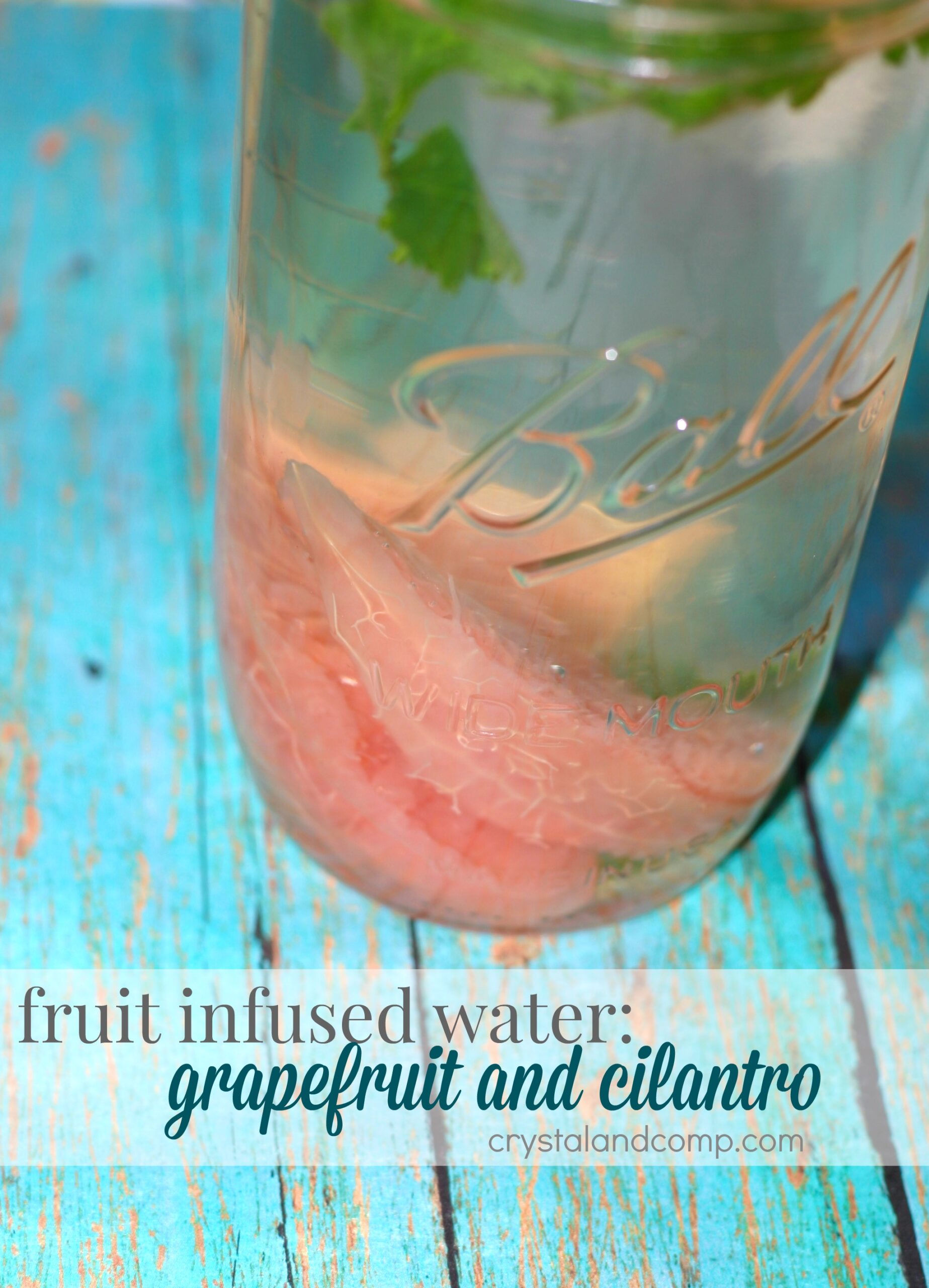 A mason jar filled with water infused with pink grapefruit slices and cilantro leaves. The jar is placed on a blue wooden surface. Text on the image reads: fruit infused water: grapefruit and cilantro.