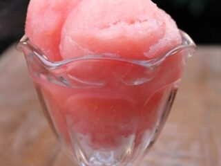 A glass dish filled with pink grapefruit sorbet, garnished with a small slice of grapefruit on top. The background is softly blurred. The text overlay at the bottom reads Grapefruit Sorbet.