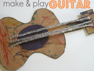 A homemade guitar craft made from cardboard. It has a colorful, scribbled body with pipe cleaner strings and is labeled make & play GUITAR at the top.