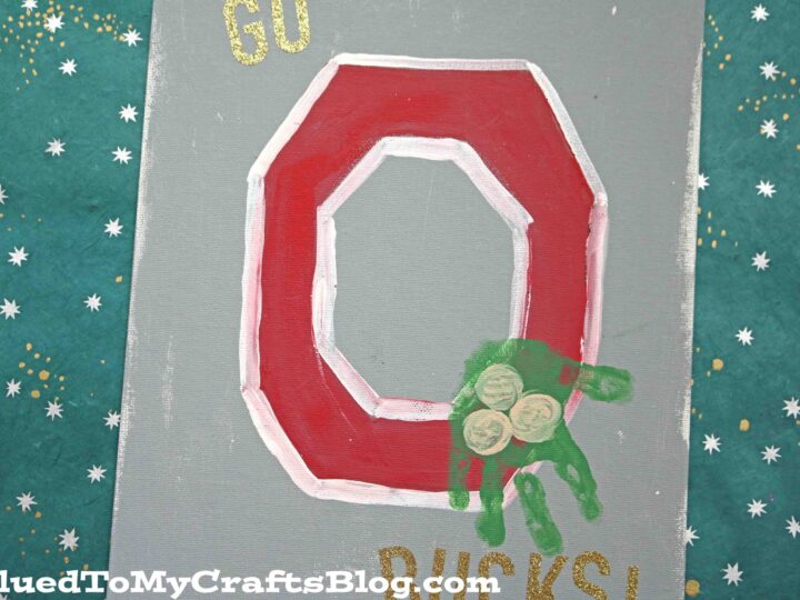 A canvas with a large red and white letter O and the words GO BUCKS! in gold. A small green handprint with football designs overlaps the letter. The background is teal with a pattern of white stars.