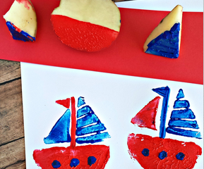 A craft project showing potato stamps used to create red and blue sailboat shapes on paper. Two painted potato halves and bottles of red and blue paint are visible. Text reads Potato Sailboats.