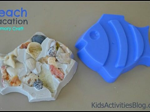 A fish-shaped craft made from assorted shells and stones beside a blue fish mold. The text reads Beach Vacation Memory Craft. Website: KidsActivitiesBlog.com.