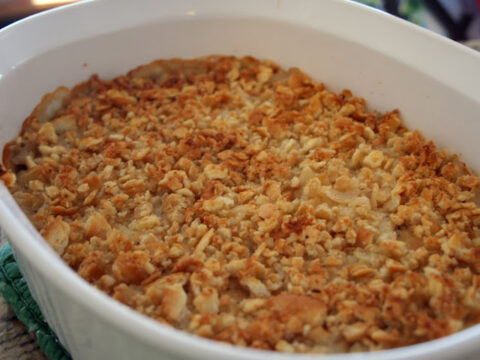 A white baking dish filled with a golden-brown casserole, topped with a crispy layer of crushed crackers or breadcrumbs, resting on a green pot holder.