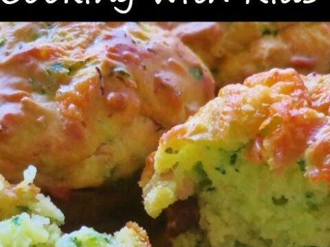Close-up of golden-brown muffins with visible green herbs baked in, suggesting a savory flavor. A black banner with white text at the top reads Cooking With Kids.