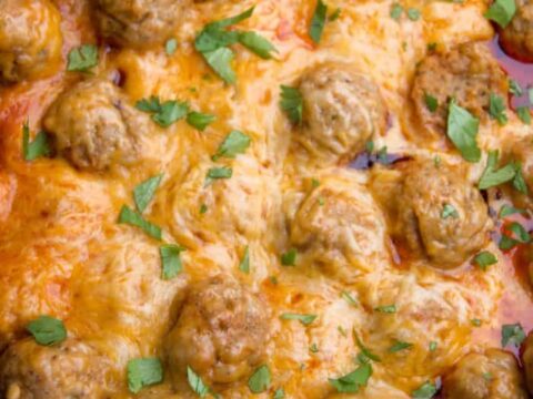 Close-up of a slow-cooked dish featuring meatballs nestled in a melted cheese and tomato sauce. The dish is garnished with chopped parsley and housed in a black cooking pot.