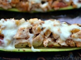 A baked zucchini boat filled with diced chicken, vegetables, and melted cheese on top. The dish is placed on a dark surface, highlighting the textures and colors of the ingredients.
