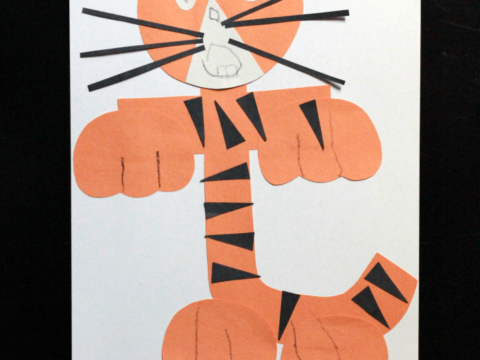 Preschool alphabet book page featuring a lowercase letter t made to look like a tiger using orange paper and black stripes, with added eyes, nose, mouth, and whiskers on a black background.