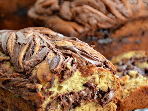Close-up of a sliced loaf of bread with swirls of melted chocolate on top and inside, resting on a cooling rack. The bread appears moist and richly textured.