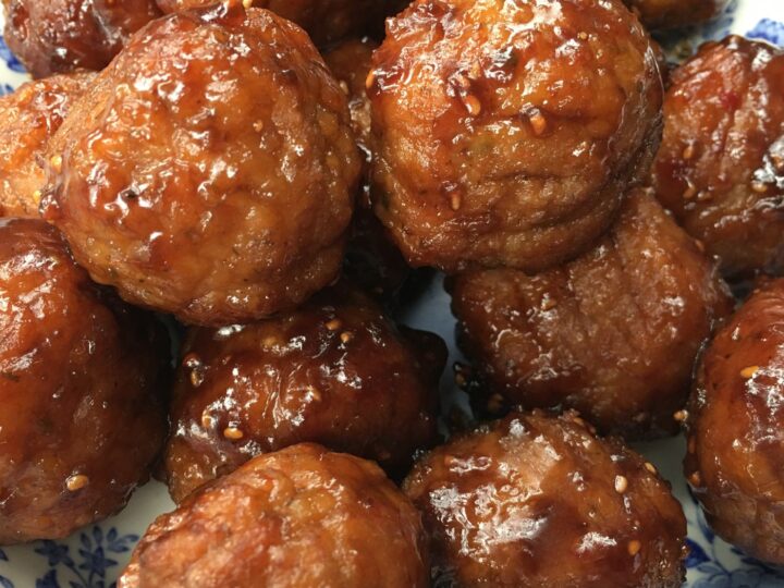 Close-up of a plate filled with glistening, sauce-covered fried meatballs. The dish is served on a blue and white patterned plate, highlighting the golden-brown color and texture of the meatballs.