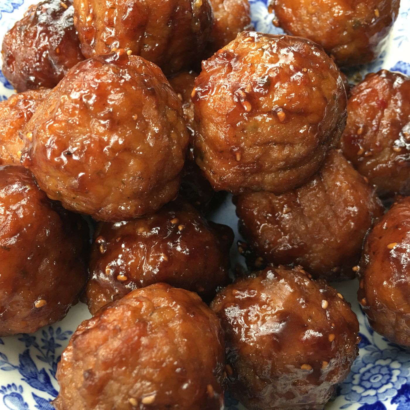 Close-up of a plate filled with glistening, sauce-covered fried meatballs. The dish is served on a blue and white patterned plate, highlighting the golden-brown color and texture of the meatballs.