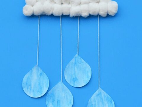 A rain cloud craft made of white cotton balls and blue watercolor paper rain drops suspended by string. The text reads Rain Cloud Craft for Kids with Bonus song! in a blue corner. A logo for The Kindergarten Connection is in the top left.