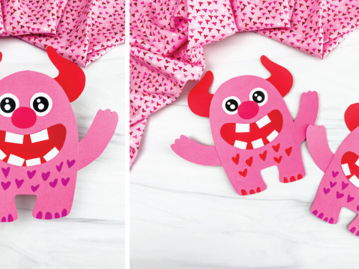 Two pink paper monsters with red horns, large eyes, and big smiles with red heart patterns on their bodies. They are placed on a white surface with pink heart-patterned fabric in the background. A hand holds one of the monsters on the left.