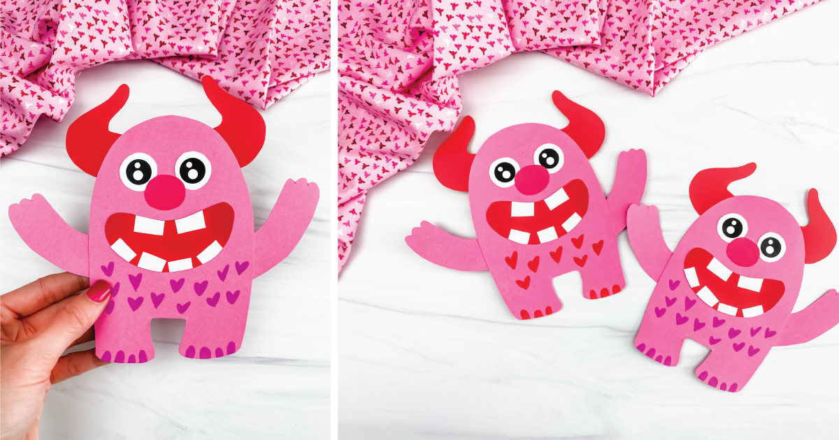 Two pink paper monsters with red horns, large eyes, and big smiles with red heart patterns on their bodies. They are placed on a white surface with pink heart-patterned fabric in the background. A hand holds one of the monsters on the left.
