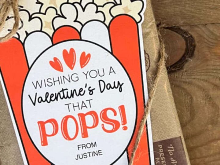A gift wrapped in brown paper with a tag showing a popcorn design. The tag reads, Wishing you a Valentines Day that pops! from Justine. The package is tied with a string on a wooden surface.