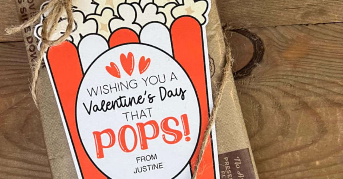 A gift wrapped in brown paper with a tag showing a popcorn design. The tag reads, Wishing you a Valentines Day that pops! from Justine. The package is tied with a string on a wooden surface.