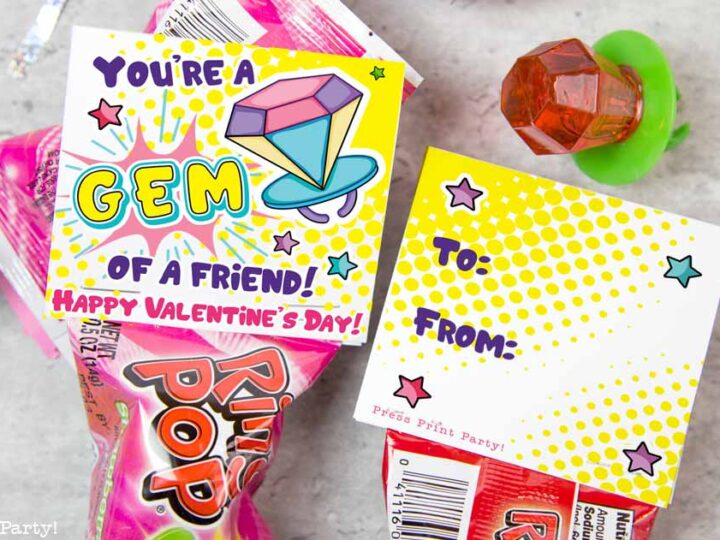 The image features a Ring Pop candy with a colorful Valentines card that says Youre a gem of a friend! Happy Valentines Day! The card has spaces labeled To: and From: surrounded by star and heart graphics. A toy ring is nearby.