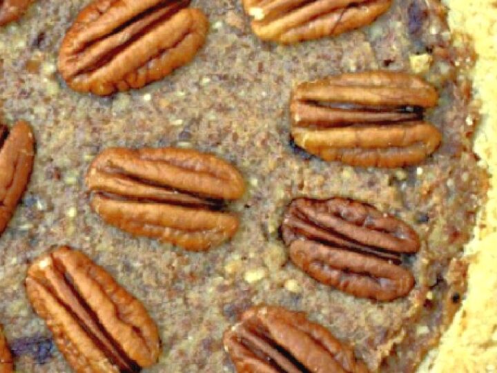 Close-up of a pecan pie with whole pecans evenly distributed on top. The filling appears rich and nutty, with a golden-brown crust visible along the edges.