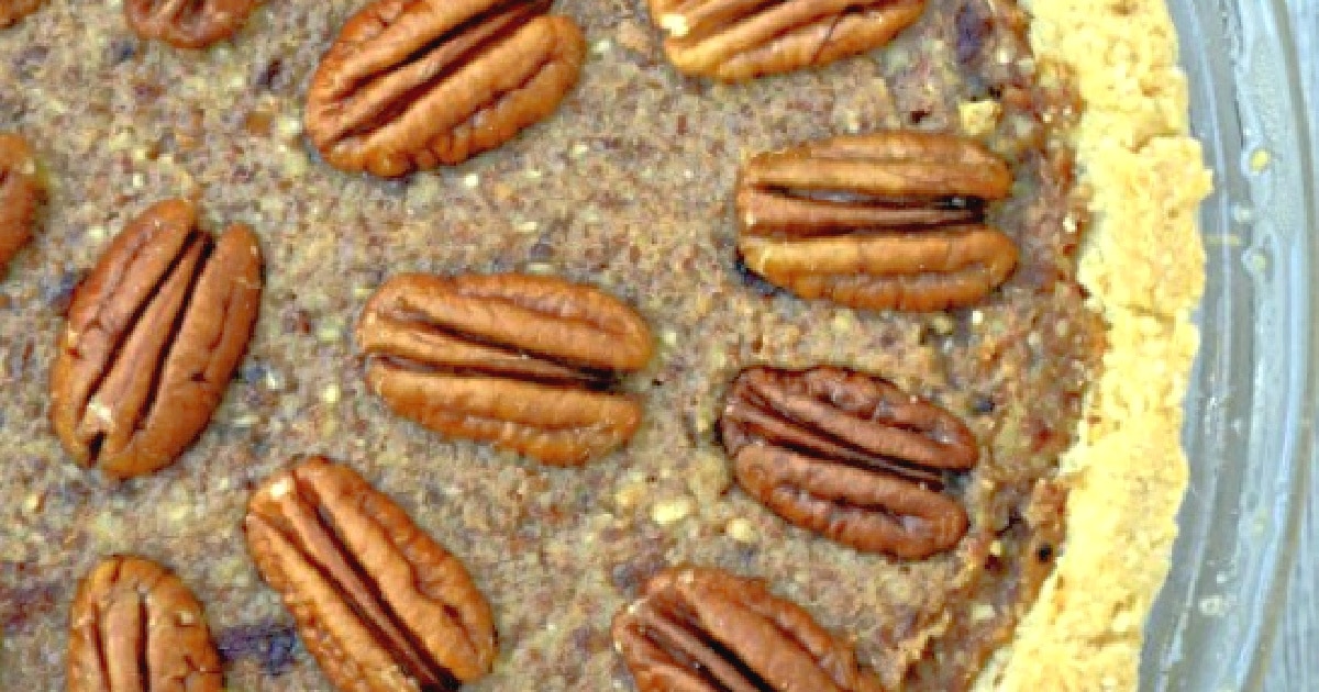 Close-up of a pecan pie with whole pecans evenly distributed on top. The filling appears rich and nutty, with a golden-brown crust visible along the edges.