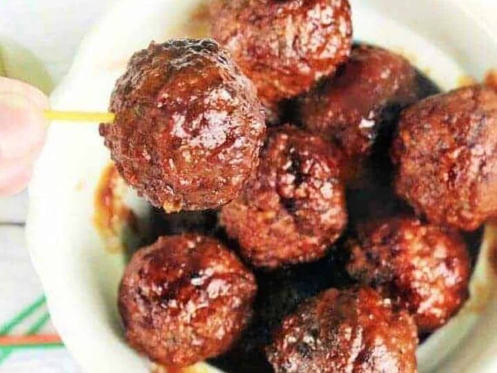 A bowl filled with glazed meatballs, with one being held up on a toothpick. The meatballs appear succulent and well-cooked, covered in a rich, shiny sauce.