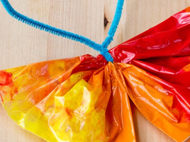 A simple butterfly craft made from a colorful painted coffee filter, pinched in the middle and tied with a blue pipe cleaner, resting on a wooden surface.
