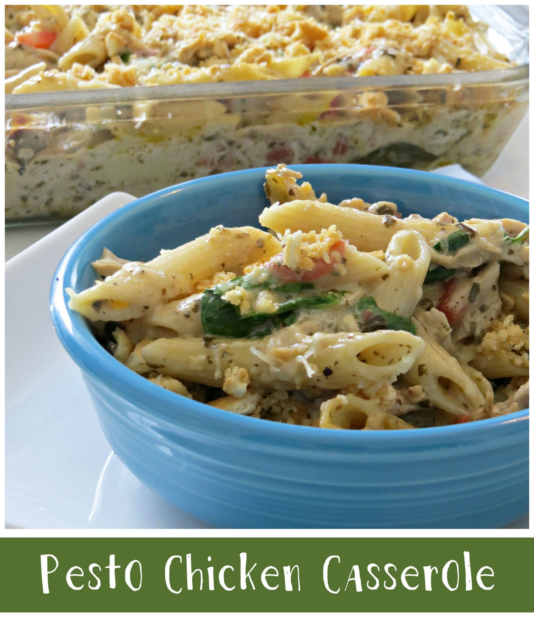 Close-up of a blue bowl filled with pesto chicken casserole, featuring penne pasta, spinach, and a creamy sauce, topped with breadcrumbs. A larger portion is in a glass baking dish in the background. Text reads Pesto Chicken Casserole at the bottom.