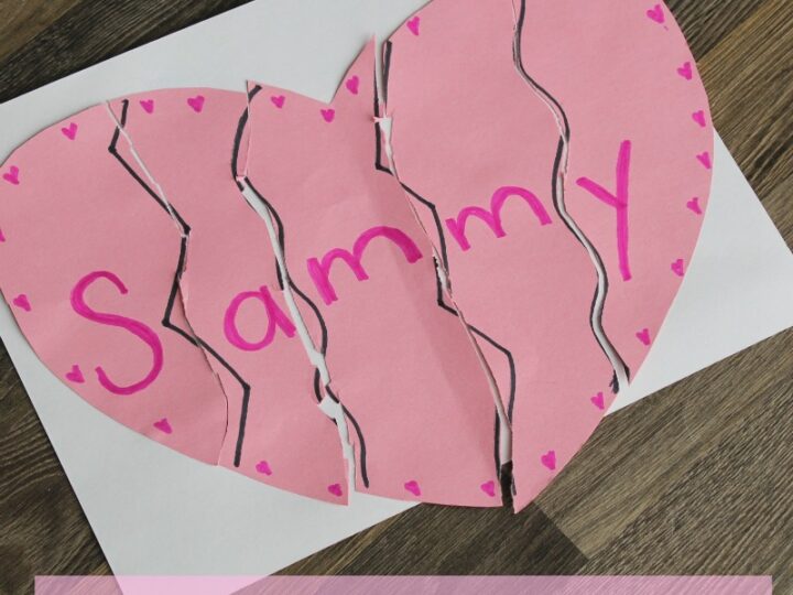 A paper heart puzzle with five pieces spells Sammy in pink. Its arranged on a white sheet, with the pieces having zigzag edges, and pink hearts are drawn around the letters. Text below reads, A Valentine Name Puzzle.