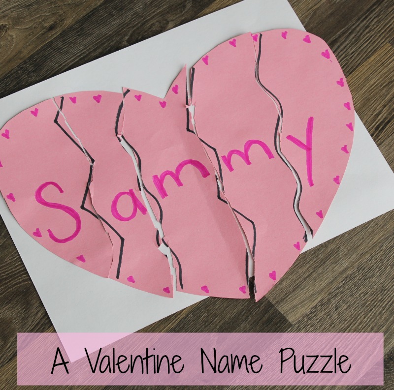 A paper heart puzzle with five pieces spells Sammy in pink. Its arranged on a white sheet, with the pieces having zigzag edges, and pink hearts are drawn around the letters. Text below reads, A Valentine Name Puzzle.