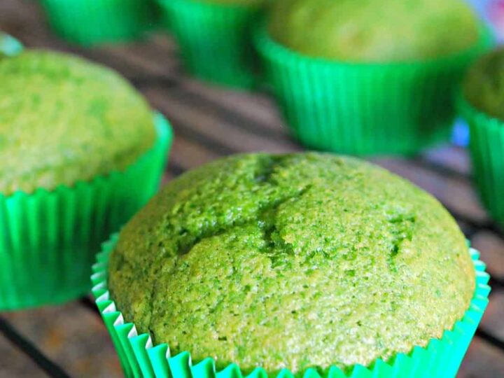 Green spinach muffins in bright green paper liners on a cooling rack, with text reading Spinach Muffins that Kids LOVE at the top. A logo mess for less appears in the bottom right corner.