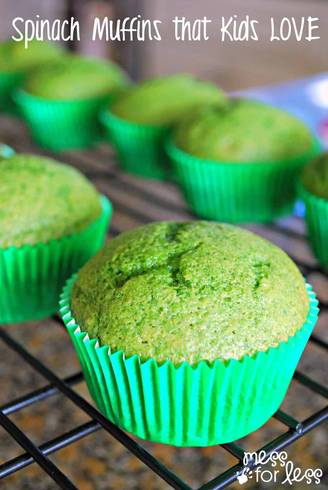 Green spinach muffins in bright green paper liners on a cooling rack, with text reading Spinach Muffins that Kids LOVE at the top. A logo mess for less appears in the bottom right corner.