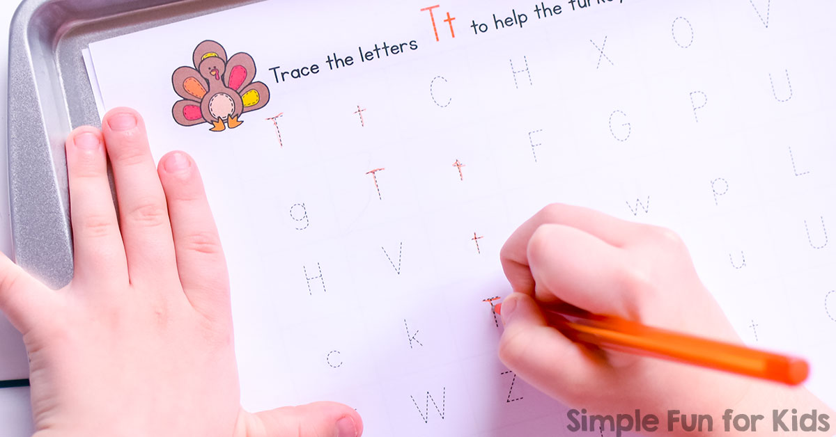 Child writing with an orange pencil on a worksheet featuring the letter T. The worksheet includes uppercase and lowercase letters with a cartoon turkey illustration. Text reads Trace the letters Tt to help the turkey.