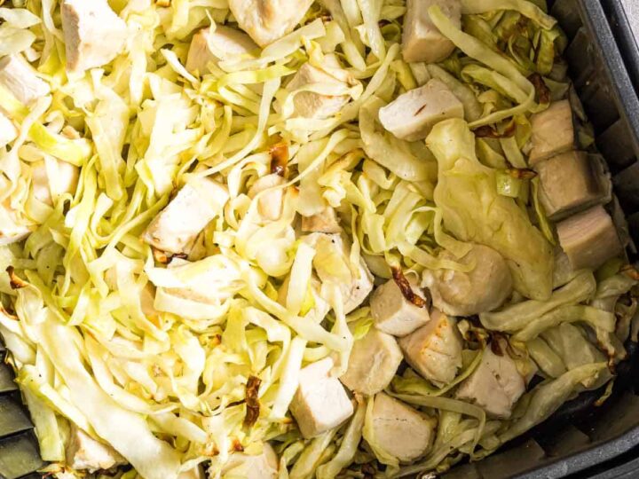 Chopped cabbage and diced chicken pieces in an air fryer basket, ready for cooking. The mixture is evenly spread, displaying a combination of pale green cabbage and lightly cooked white chicken chunks.