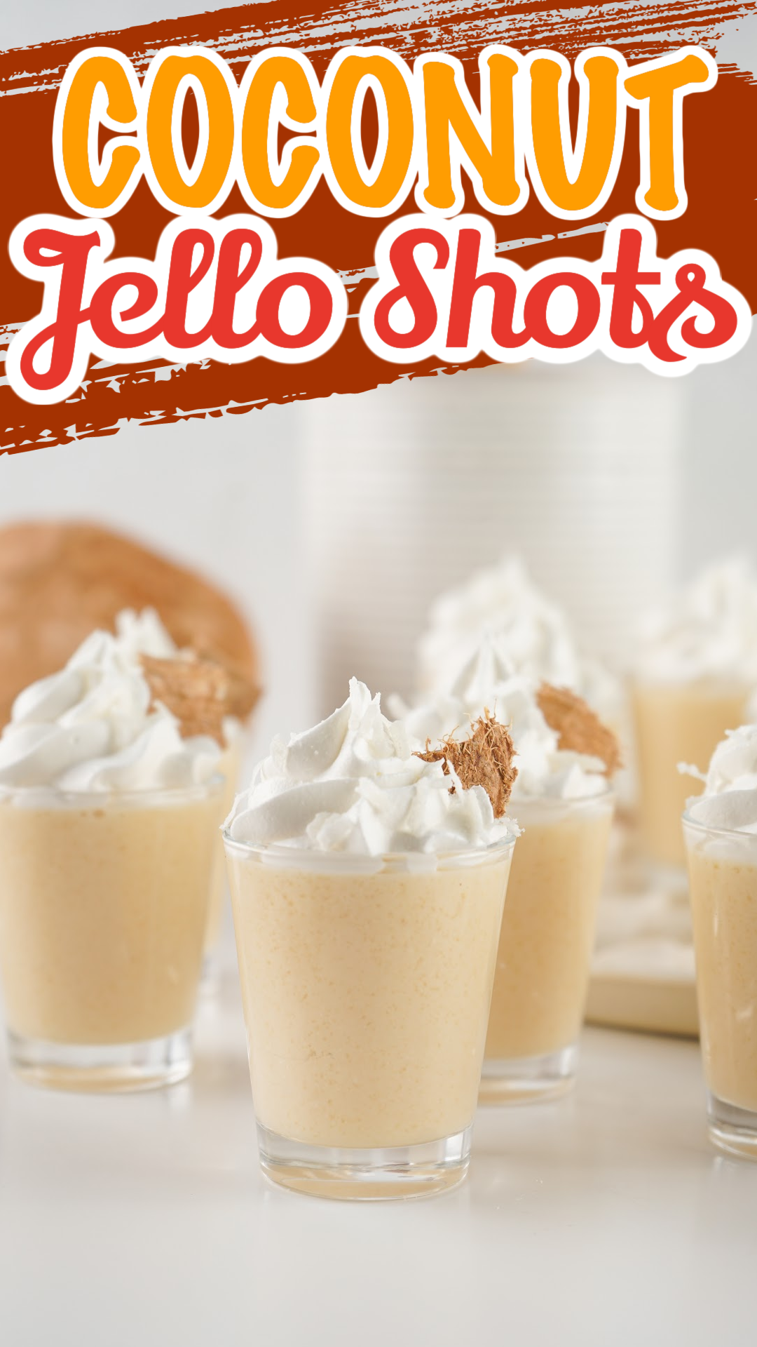 Five small dessert cups filled with creamy coconut jello shots, each topped with whipped cream and a sprinkle of brown crumb. The background features a coconut and stacks of paper cups. The text at the top reads Coconut Jello Shots.
