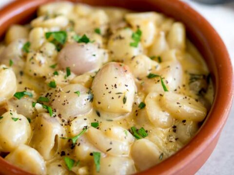 A terracotta bowl filled with creamy mushroom stew garnished with chopped parsley and freshly ground black pepper. The dish is rich and hearty, featuring small, round mushrooms in a thick, savory sauce.