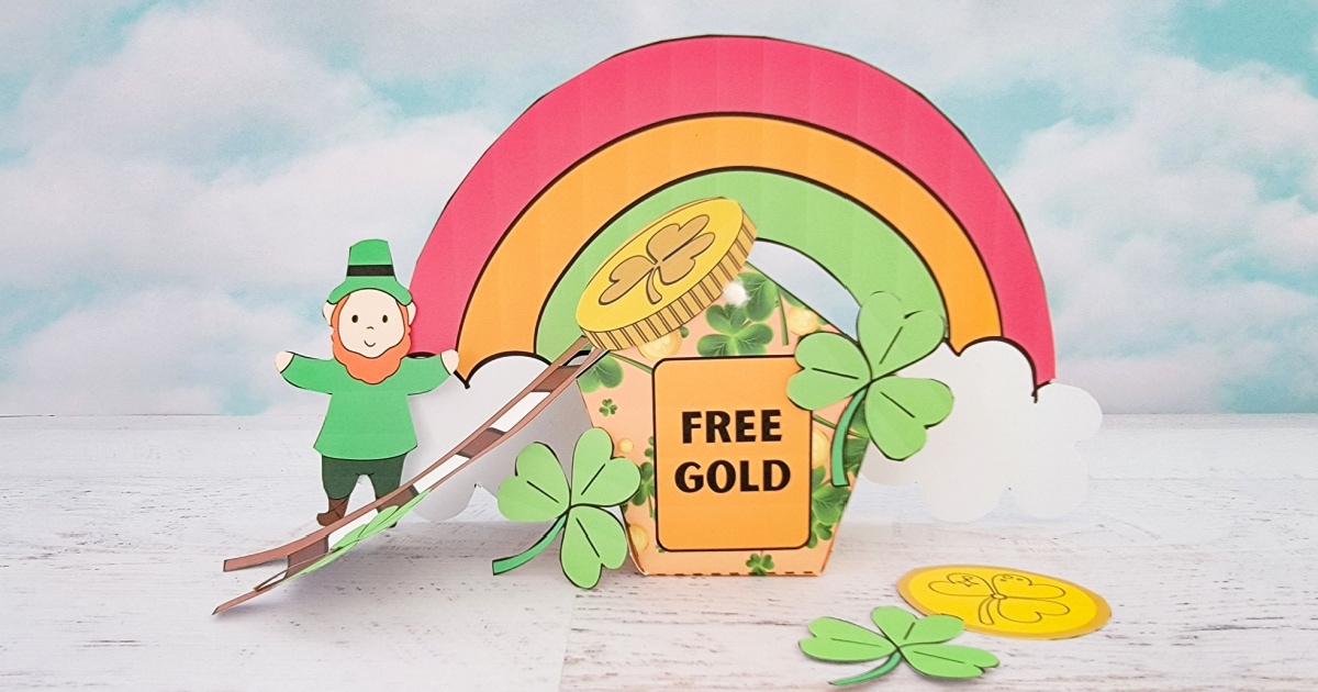 A paper craft scene with a leprechaun standing on a rainbow leading to a jar labeled Free Gold. Shamrocks are scattered around, and white clouds frame the rainbow against a cloudy sky backdrop.
