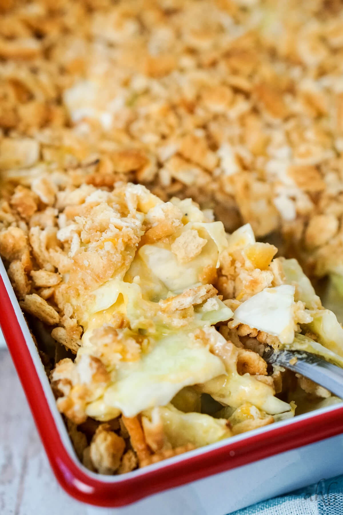 A close-up of a casserole dish filled with creamy, baked cabbage casserole topped with a golden, crunchy crust. A serving spoon is lifting a portion, revealing the creamy layers beneath the crust. The dish sits on a light-colored surface.