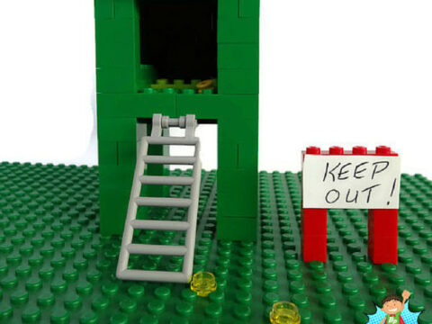 Image of a LEGO leprechaun trap featuring a green structure with a yellow top and a ladder. A small sign next to it reads Keep Out! The text above says Make a LEGO Leprechaun Trap and below is the website BrainPowerBoy.com.