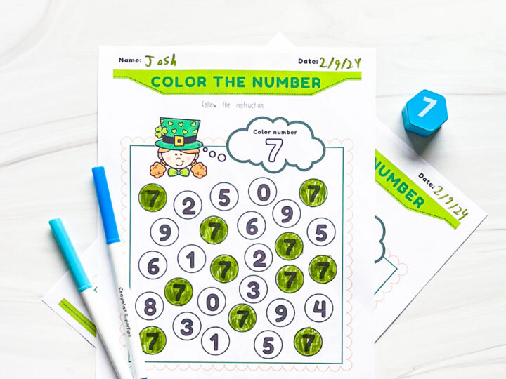 The image shows a worksheet titled Color the Number with a frog illustration at the top. The number 7 is highlighted. Several circles with numbers are marked with a green crayon. Two markers and a blue dice with the number 7 are beside the sheet.