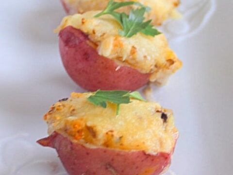 Three halved red potatoes topped with melted cheese and garnished with parsley, arranged in a row on a white surface.