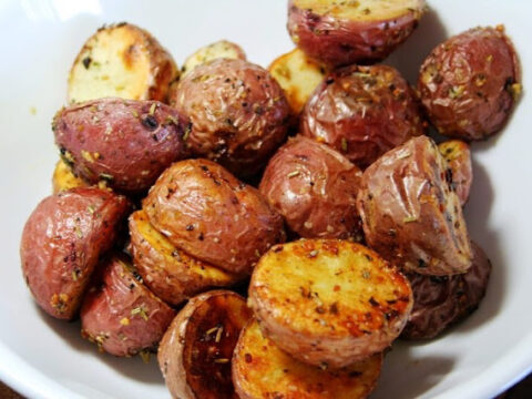 A white bowl filled with roasted baby potatoes, seasoned with herbs and spices, showcasing a crispy golden-brown exterior.