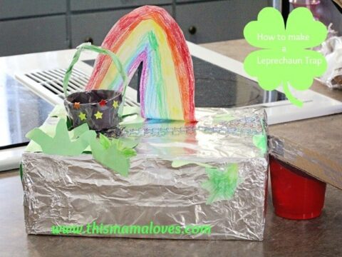 A homemade leprechaun trap made from a foil-covered box. It features a colorful rainbow leading to a black pot with stars, surrounded by green shamrocks. A small sign reads, How to make a Leprechaun Trap.