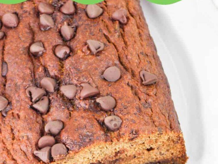 A loaf of avocado banana bread topped with chocolate chips on a white plate. Two slices are partially cut from the loaf. The top section of the image contains the text Avocado Banana Bread and the website messforless.net.