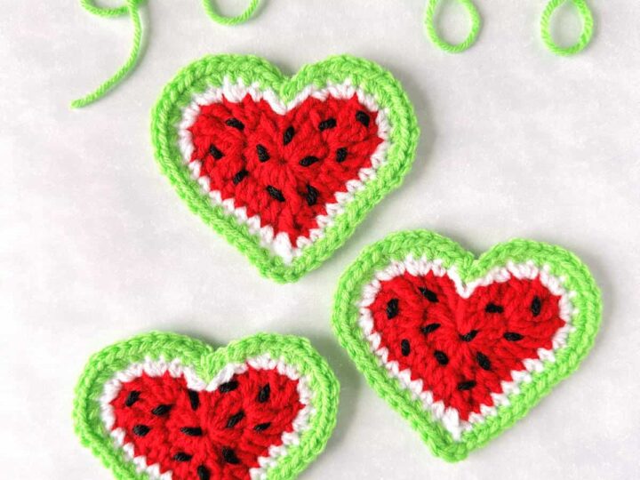 Three crochet hearts resembling watermelon slices with red centers, black seeds, and green rinds. The background is light, and a green yarn swirl is at the top. The text GoldenLucyCrafts appears at the bottom.
